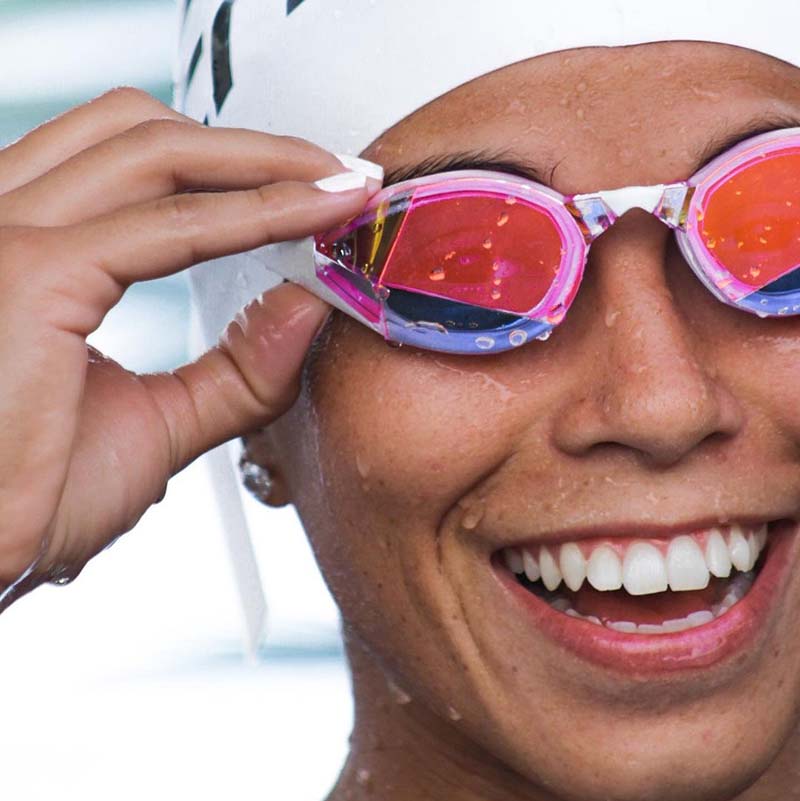 Smiling swimmer wearing THEMAGIC5 Vector Pink Magic Mirror Gold custom-fit mirrored swimming goggles during training.