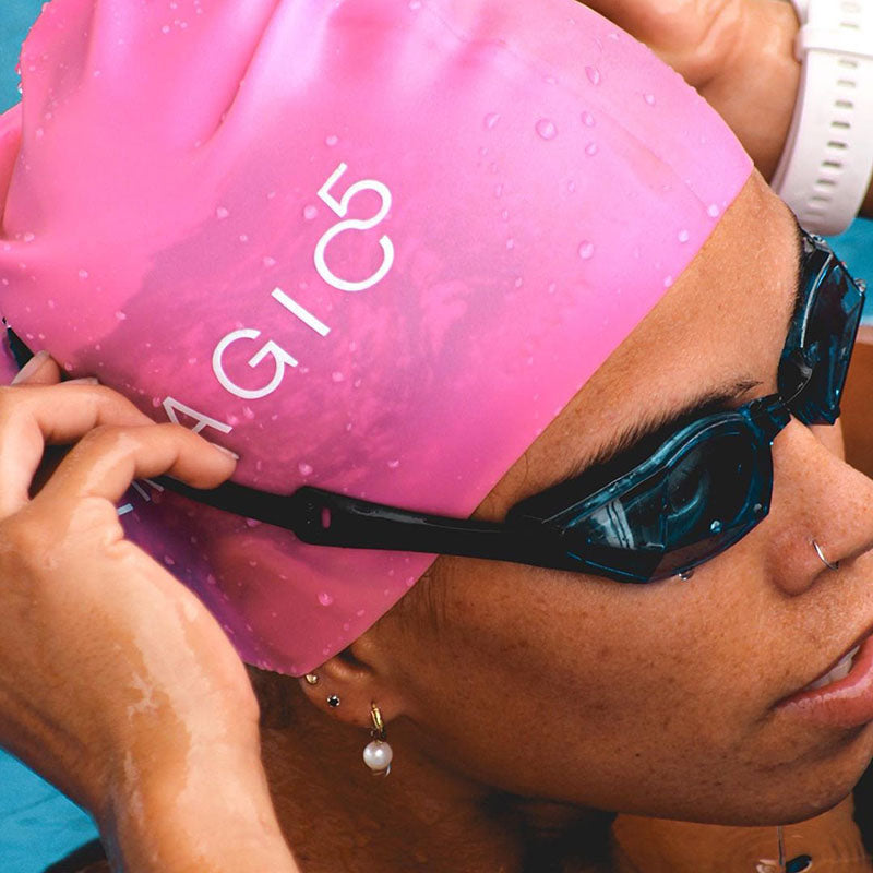 Swimmer adjusting black swim goggles while wearing a pink THEMAGIC5 swim cap