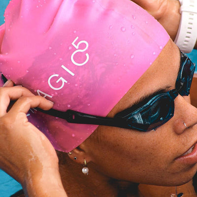 Swimmer adjusting black swim goggles while wearing a pink THEMAGIC5 swim cap