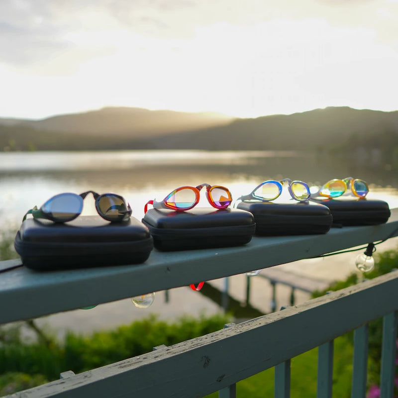 Four magic 5 goggles on the top of the magic 5 goggle cases on a railing witha a scenery background with a lake.