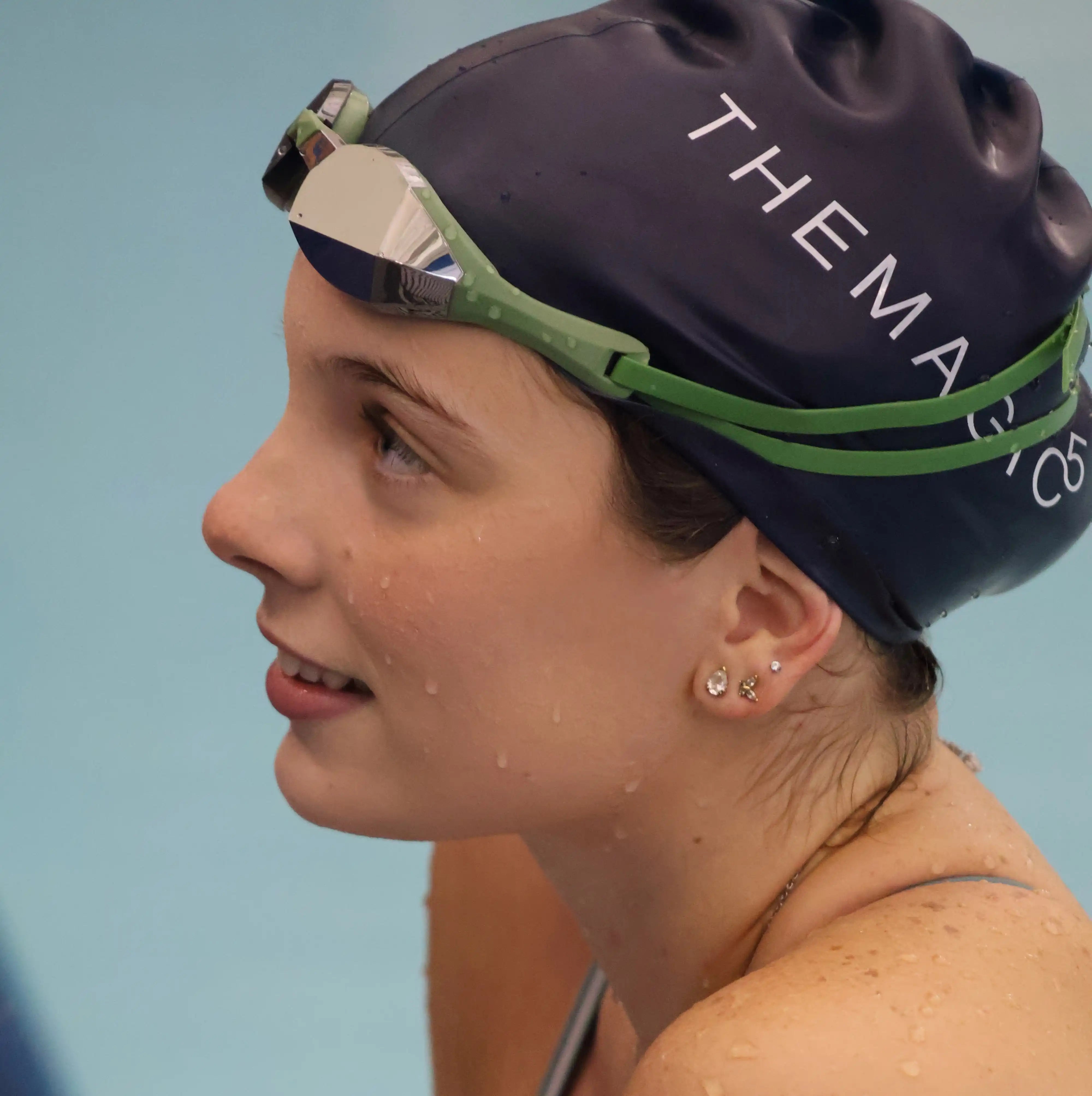 A close-up side profile of a woman in a swimming pool wearing a limited edition green silver goggles