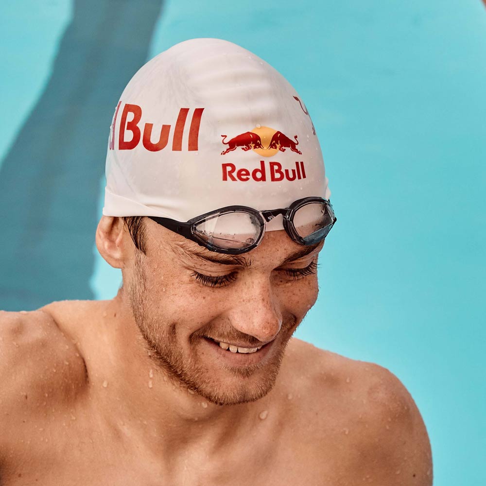 Swimmer smiling poolside with swim goggles resting on a swim cap