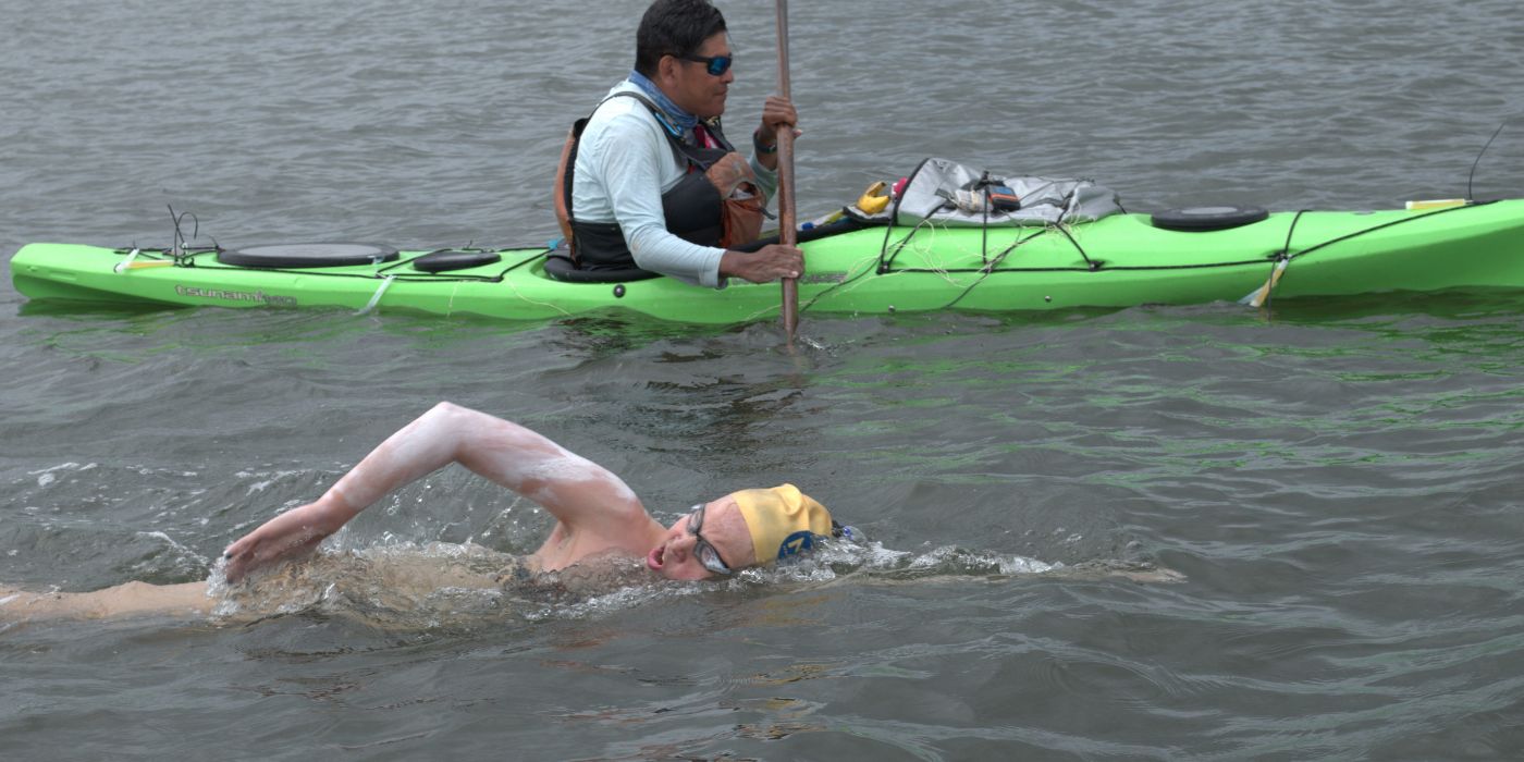 Leslie Hamilton swimming in clear magic goggles beside a Kayak