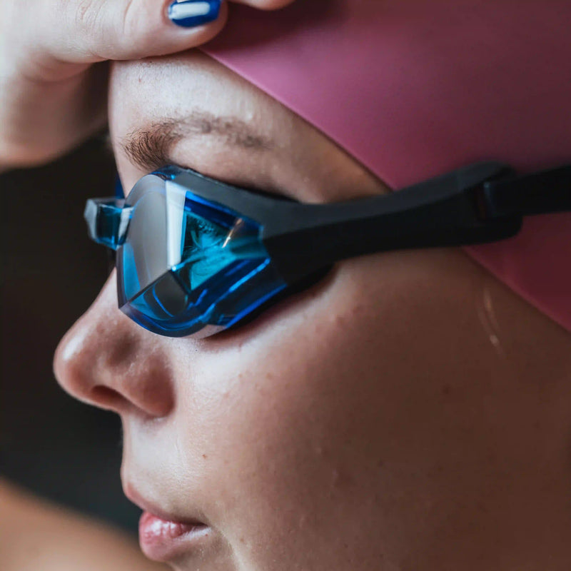 Female swimmer wearing Vector Blue Magic custom-fit swimming goggles by THEMAGIC5 with blue mirrored lenses designed for competitive swim training and leak-resistant comfort.
